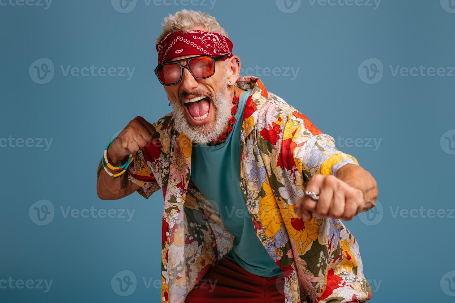 Cool hipster senior man in stylish funky shirt gesturing and shouting against blue background photo