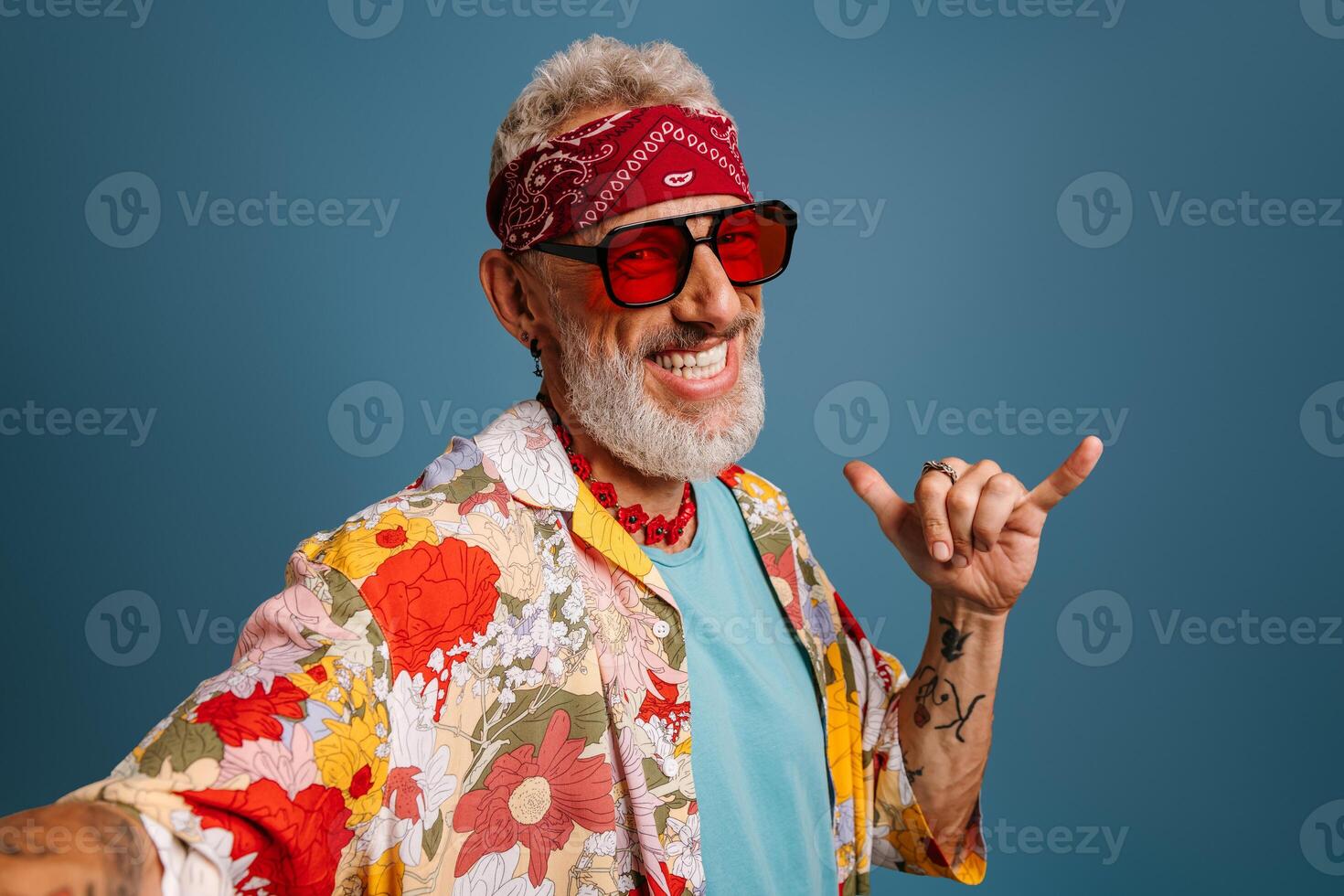 Hipster senior man in stylish funky shirt and trendy glasses making selfie and gesturing on blue background photo