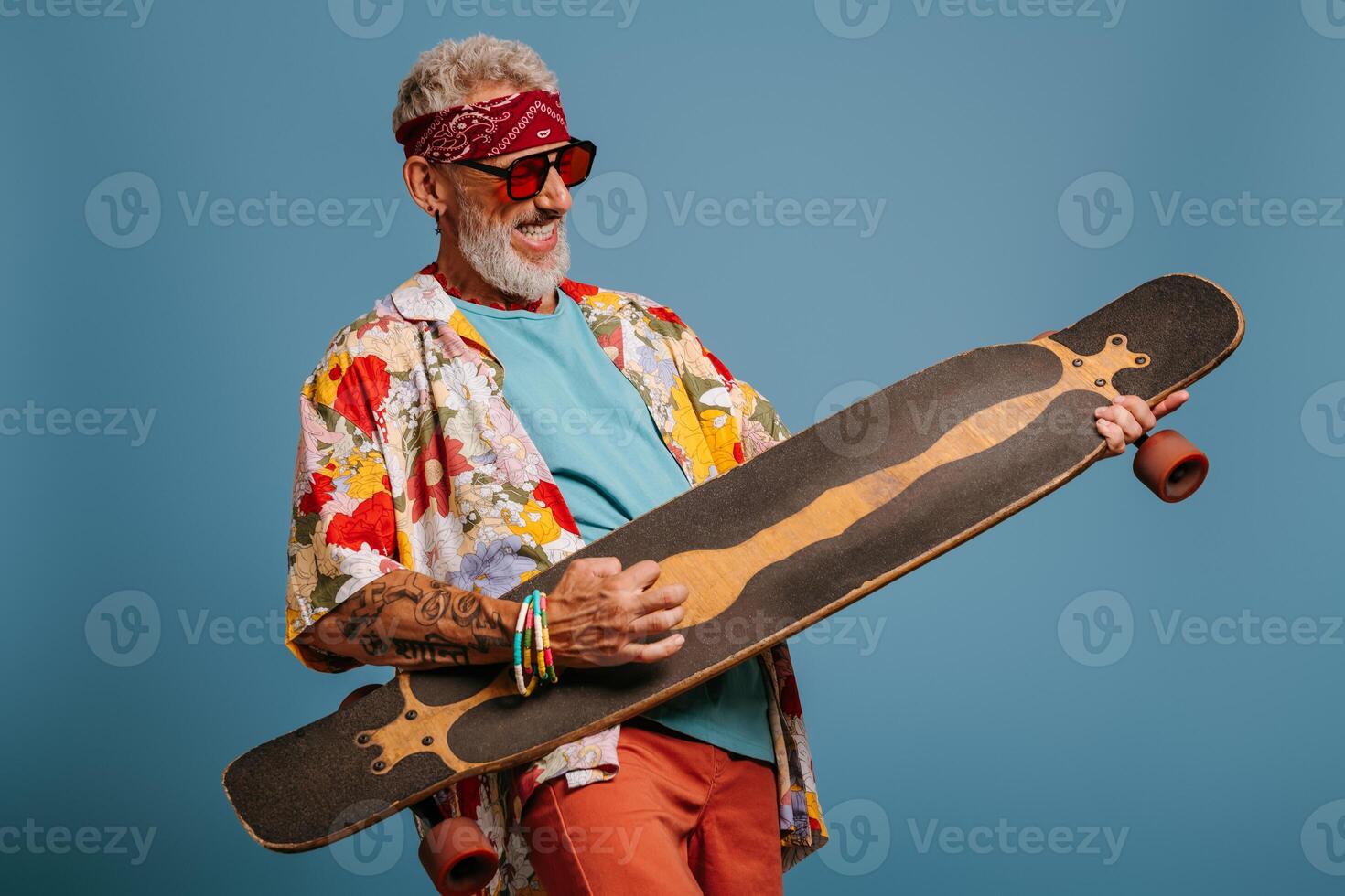 Playful senior man carrying longboard like a guitar and feeling like a rock star against blue background photo