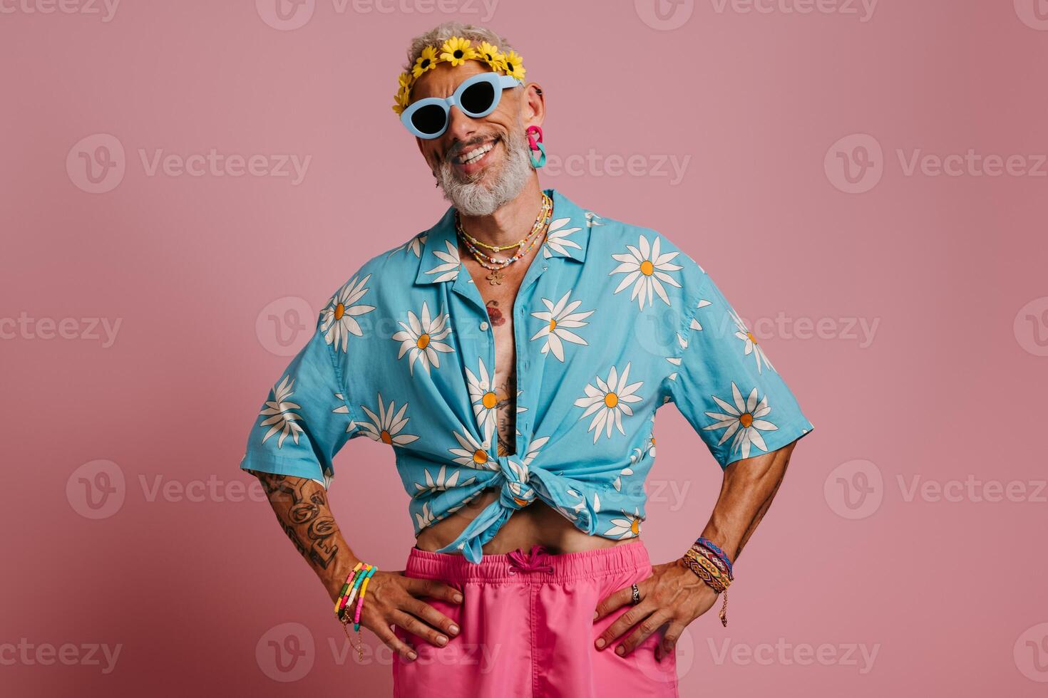 Bearded gay man in stylish shirt and floral wreath on head smiling against pink background photo