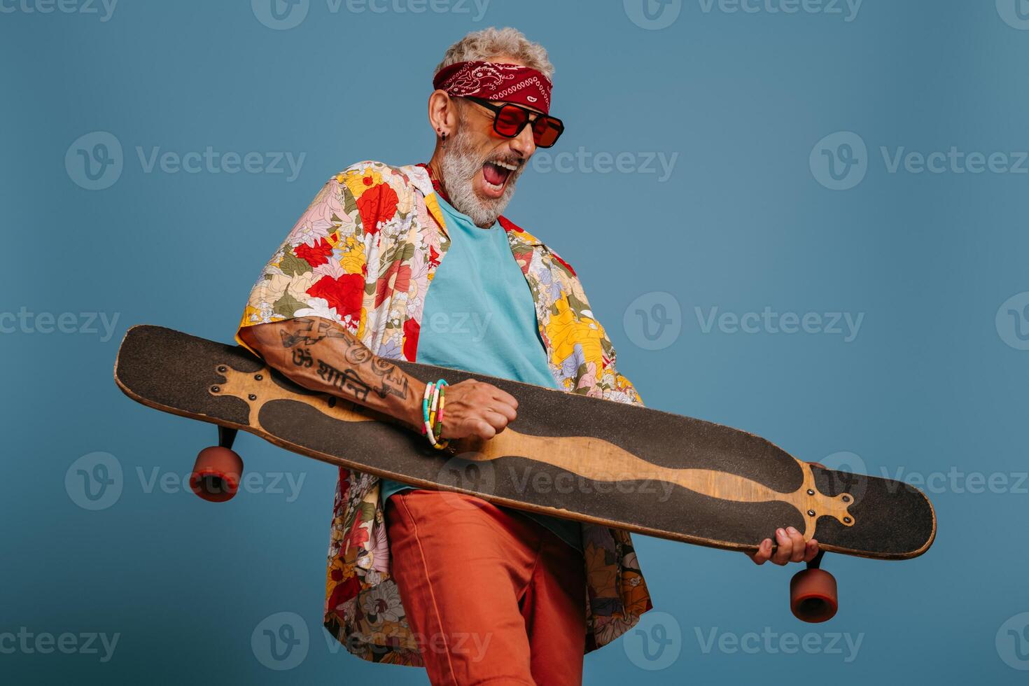 Playful senior man carrying longboard like a guitar and feeling like a rock star against blue background photo