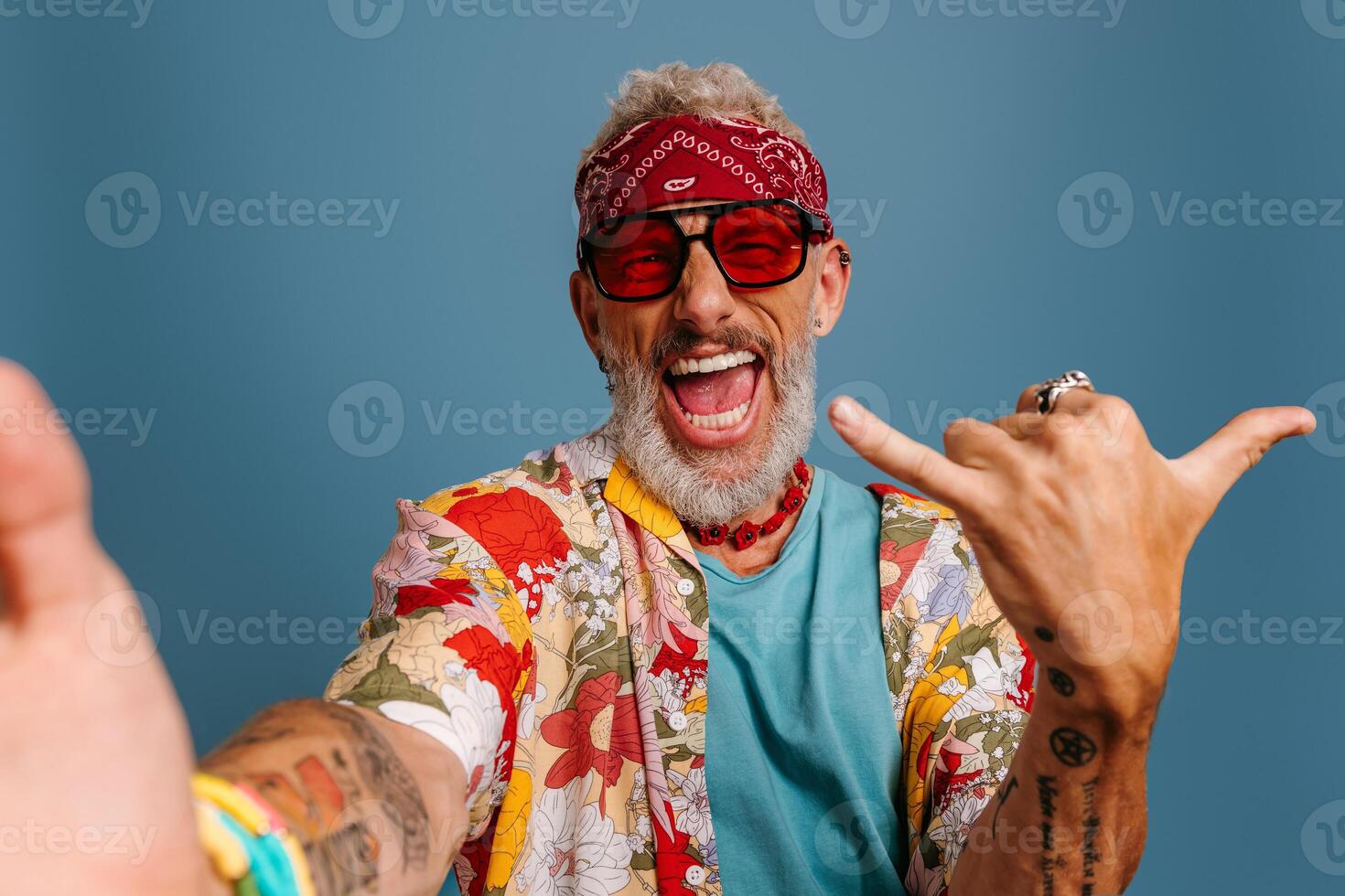 Cool senior man in stylish funky shirt and trendy glasses making selfie and gesturing on blue background photo
