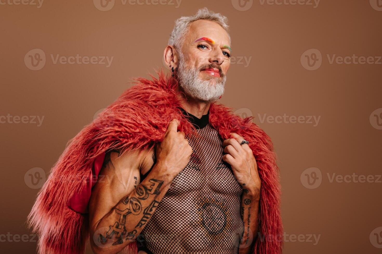 Mature gay man with rainbow colored eyebrows wearing fluffy coat against brown background photo