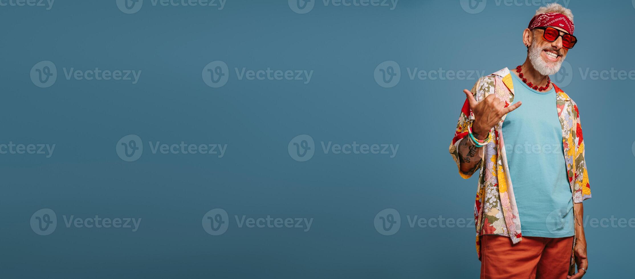 Cool hipster senior man in stylish funky shirt gesturing and smiling against blue background photo