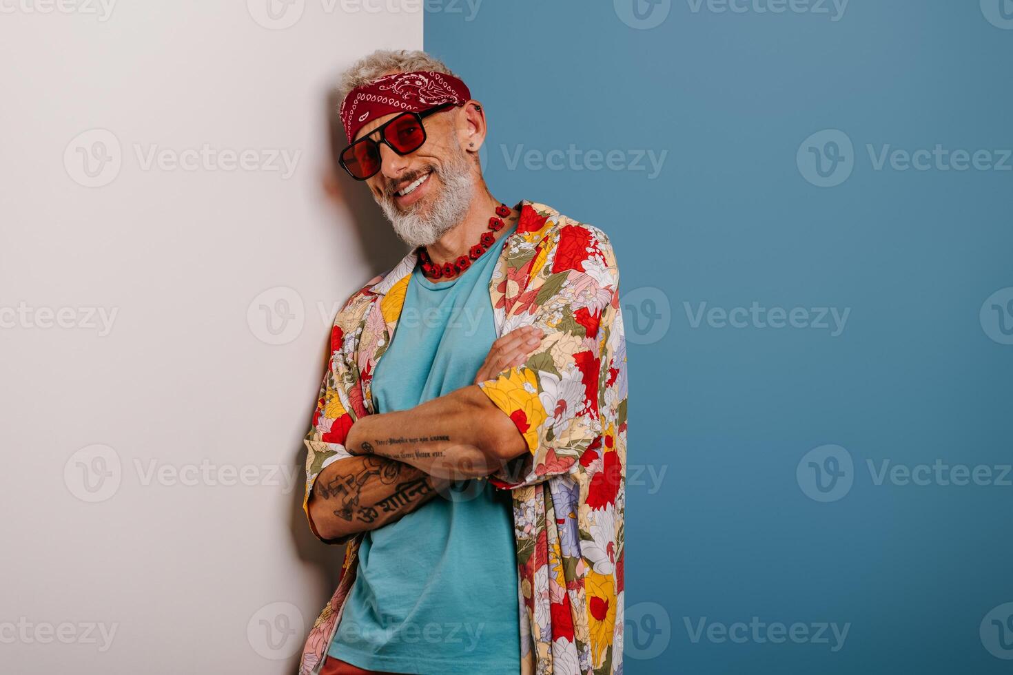 Happy senior man in stylish funky shirt leaning at copy space while standing against blue background photo