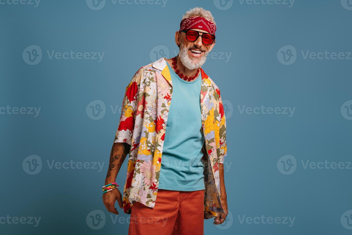 Hipster senior man in stylish funky shirt and trendy glasses smiling against blue background photo