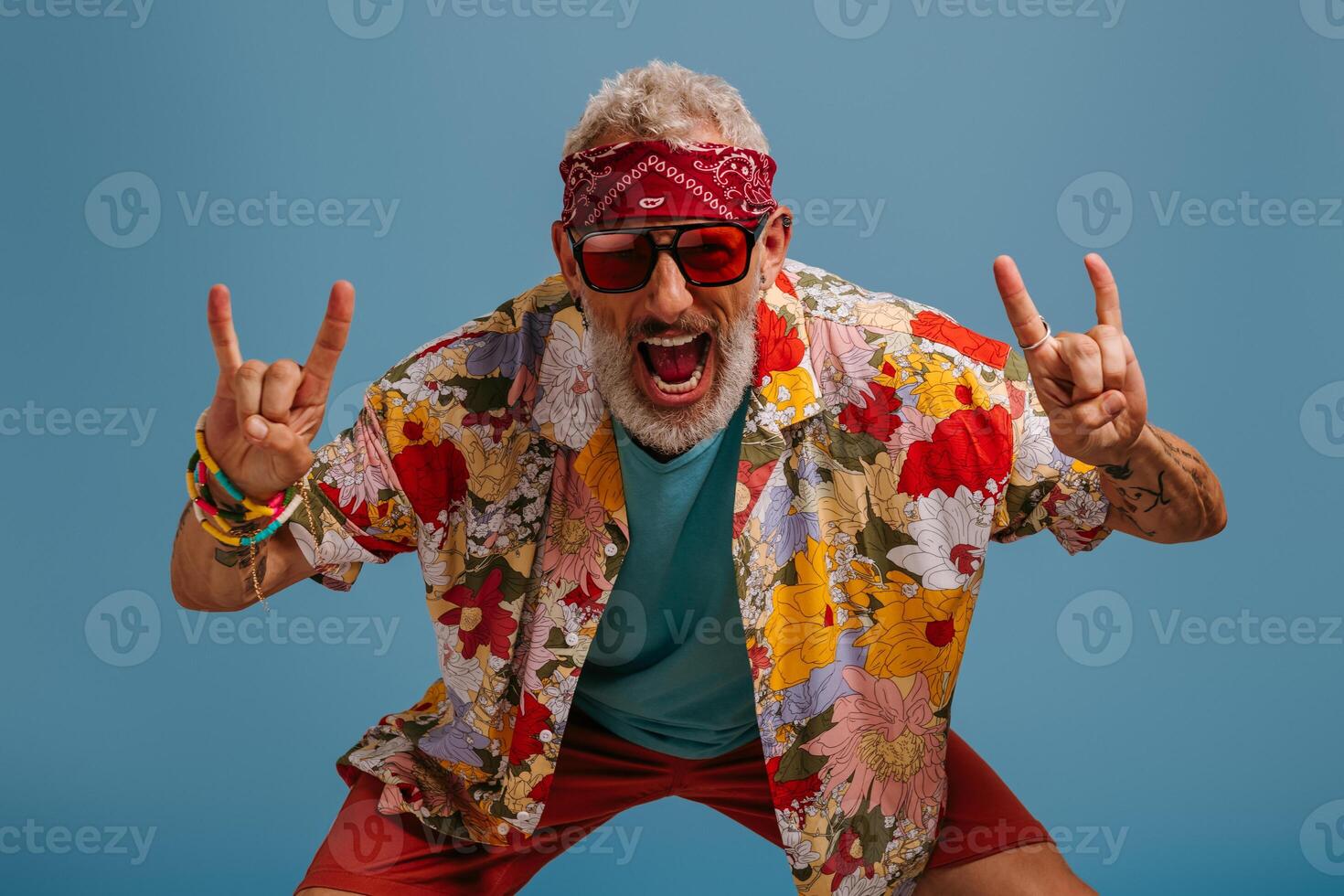 Cool hipster senior man in stylish funky shirt gesturing and smiling against blue background photo