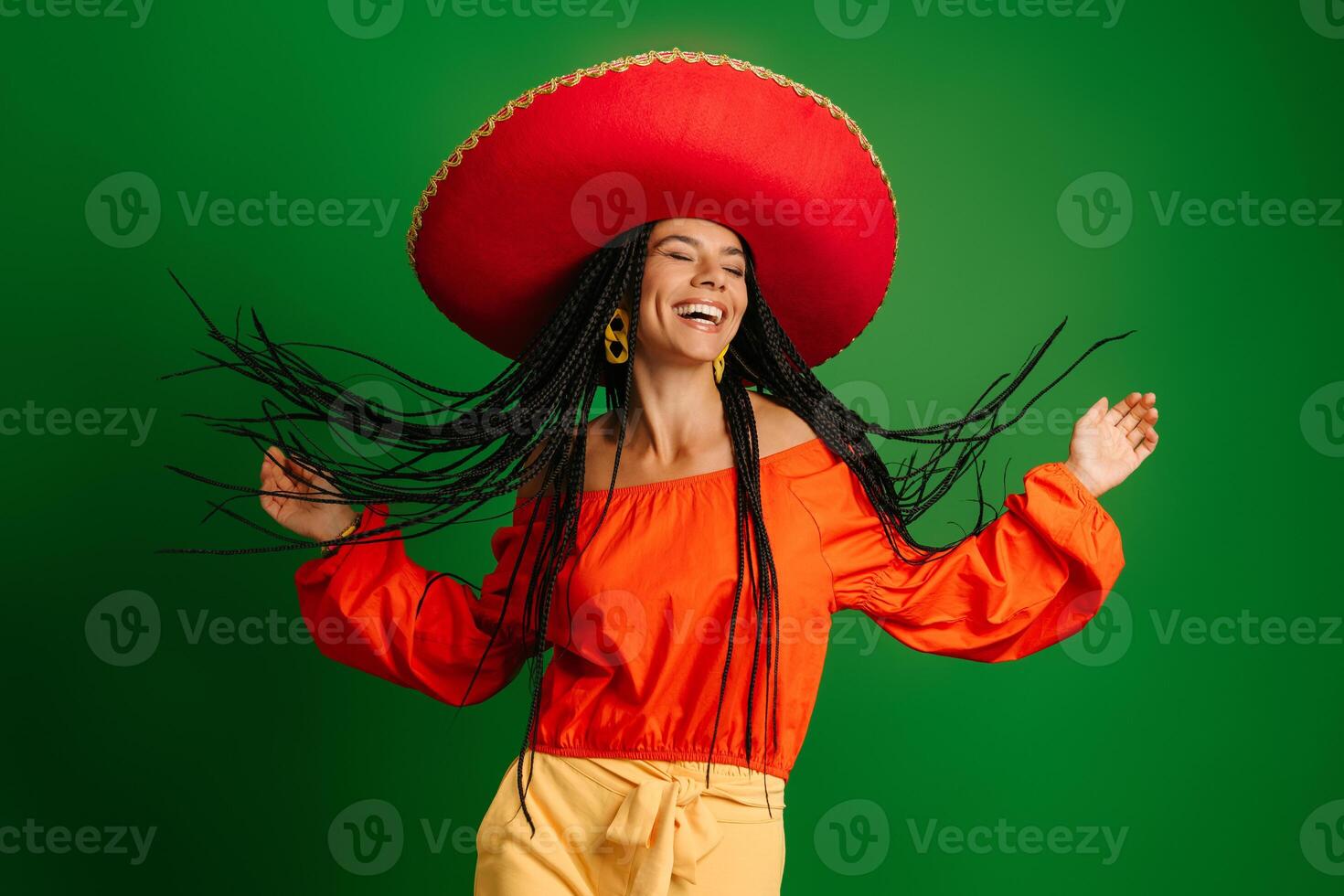 Joyful young Mexican woman in Sombrero looking happy while dancing against green background photo