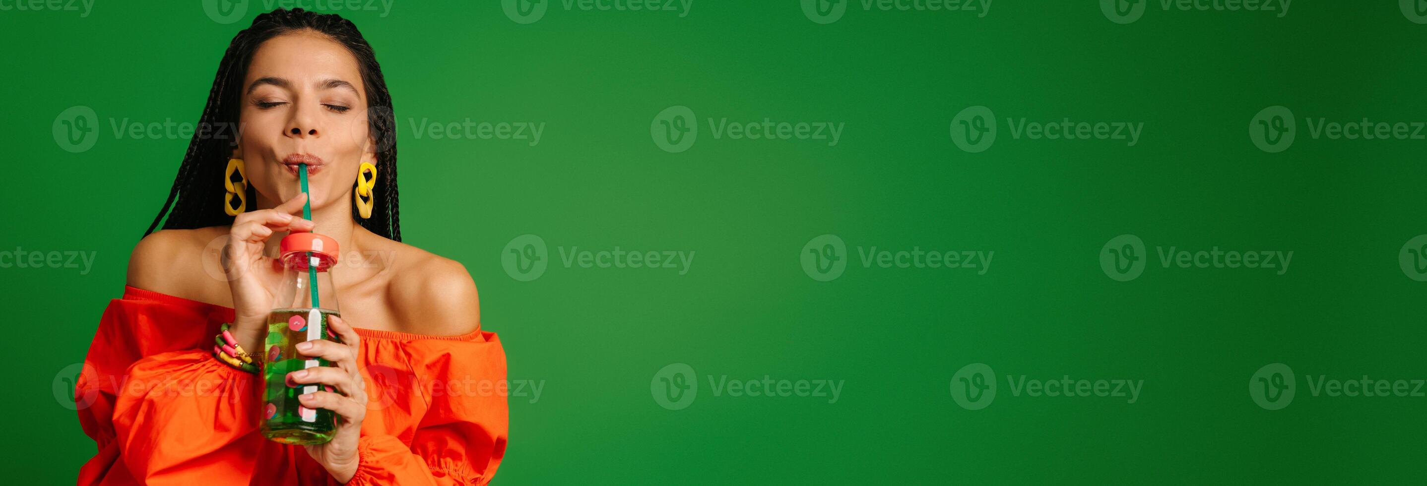 Attractive young woman enjoying fresh lemonade and keeping eyes closed against green background photo