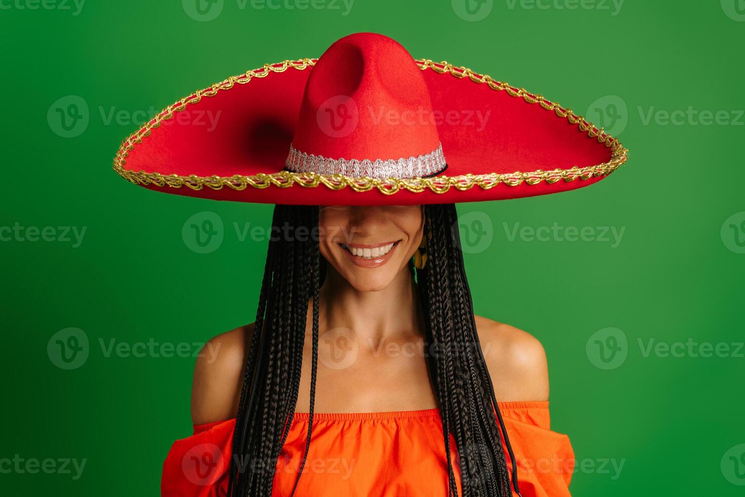 Gorgeous young Mexican woman covering half face with Sombrero and smiling against green background photo