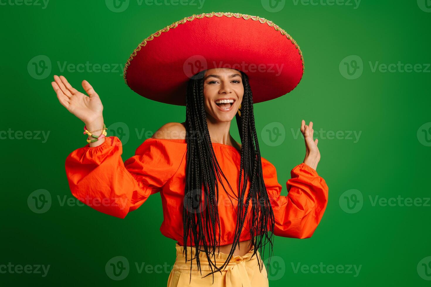 Attractive young Mexican woman in Sombrero looking happy while dancing against green background photo