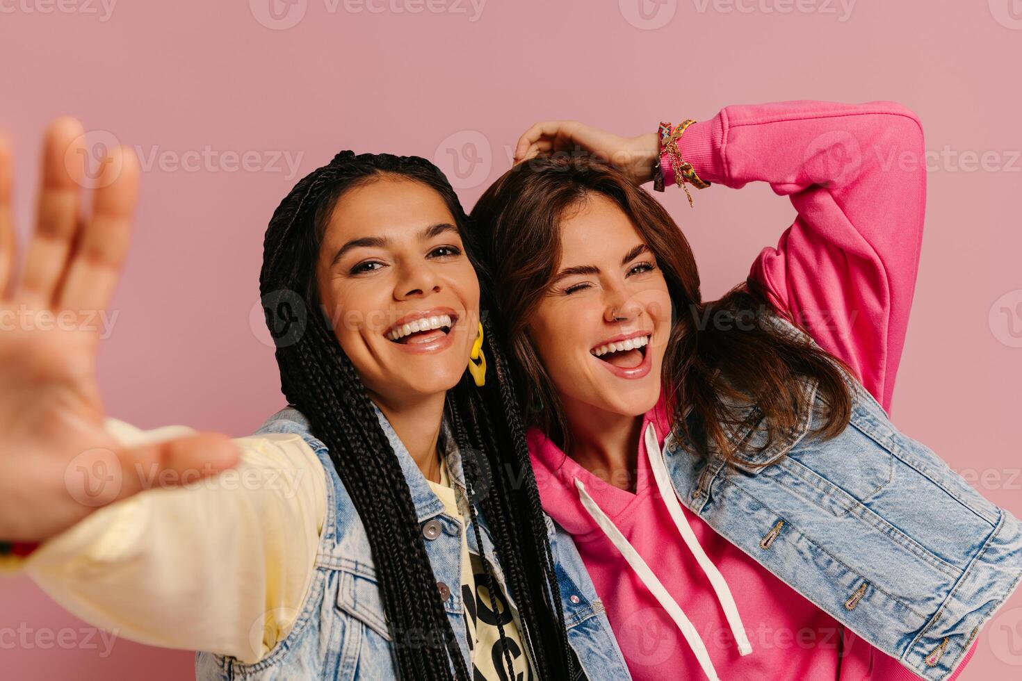 Two joyful young women in colorful wear embracing and smiling against pink background together photo