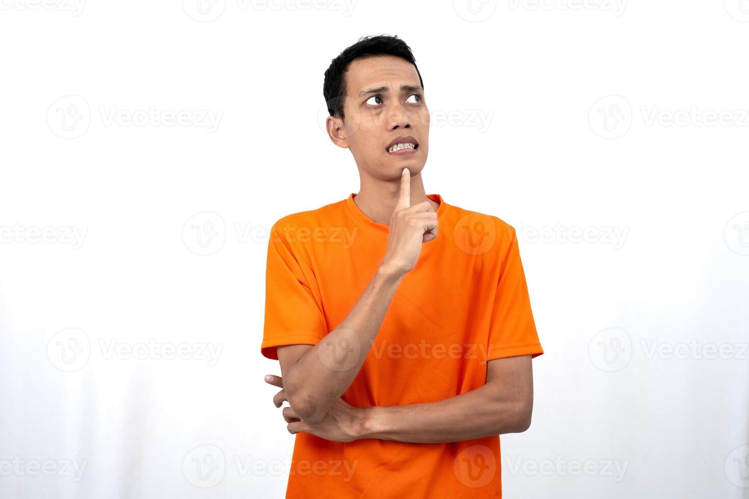 Portrait of a young Asian man wearing an orange t-shirt posing thinking, searching for ideas, or confused. Isolated on white background. photo