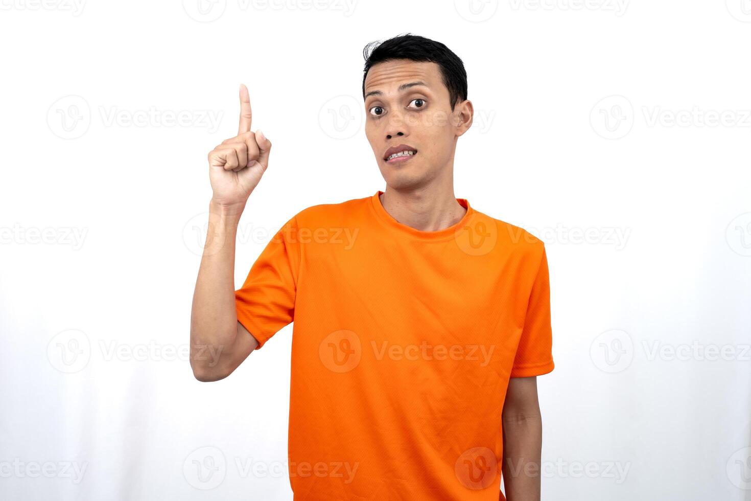 Portrait of a young Asian man wearing an orange t-shirt pointing upwards at copy space for promotional space. isolated on white background. photo