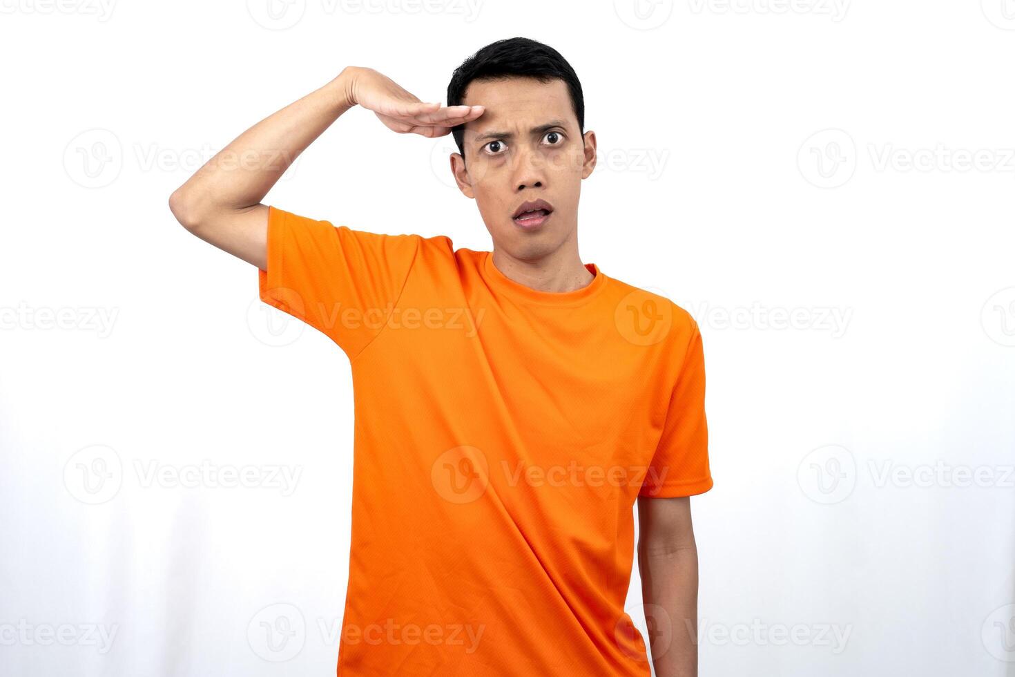 Portrait of a young Asian man wearing an orange t-shirt looking surprised, shocked and shocked. Hands are near eyes, isolated on white background. photo