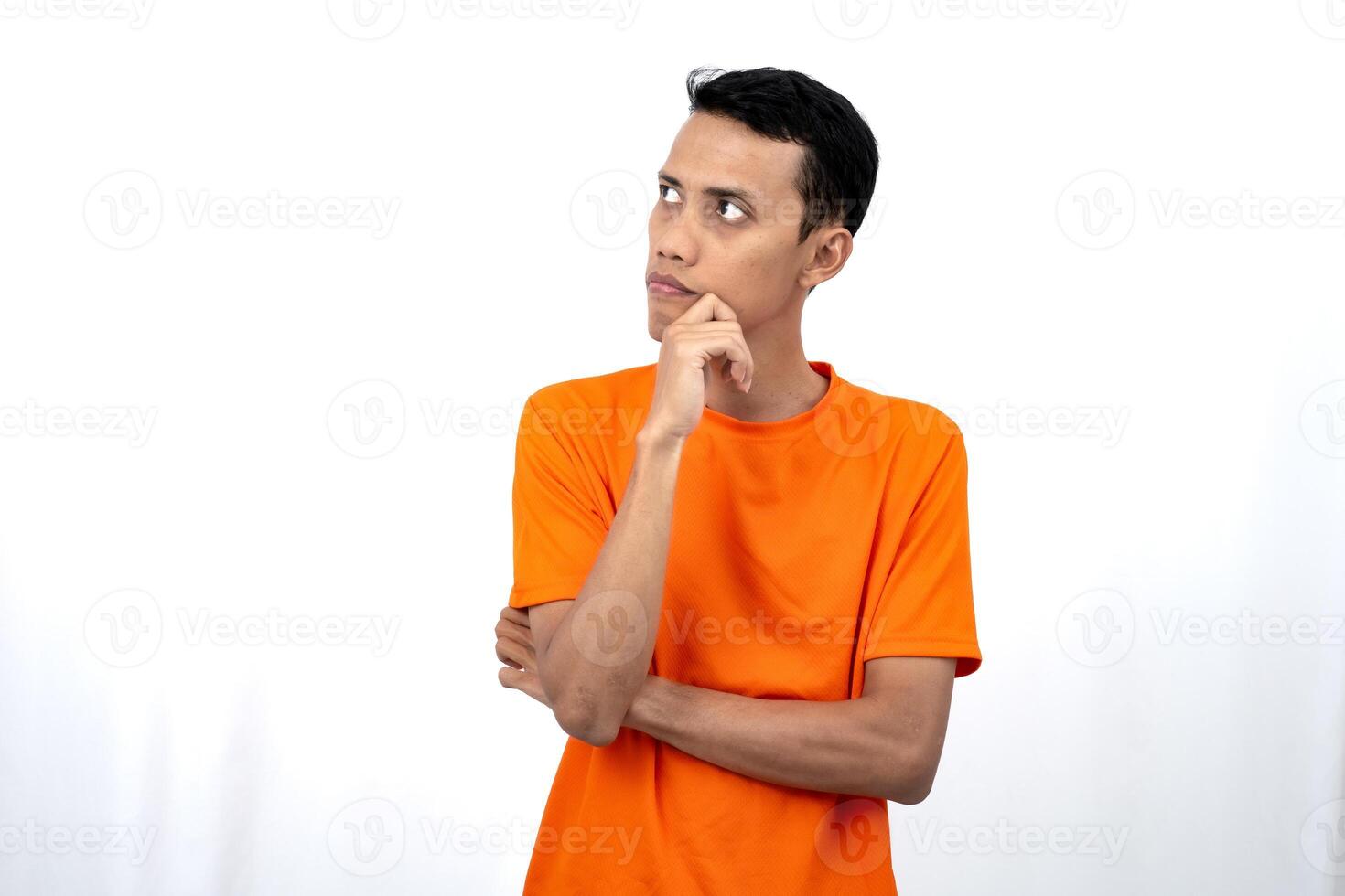 Portrait of a young Asian man wearing an orange t-shirt posing thinking, searching for ideas, or confused. Isolated on white background. photo