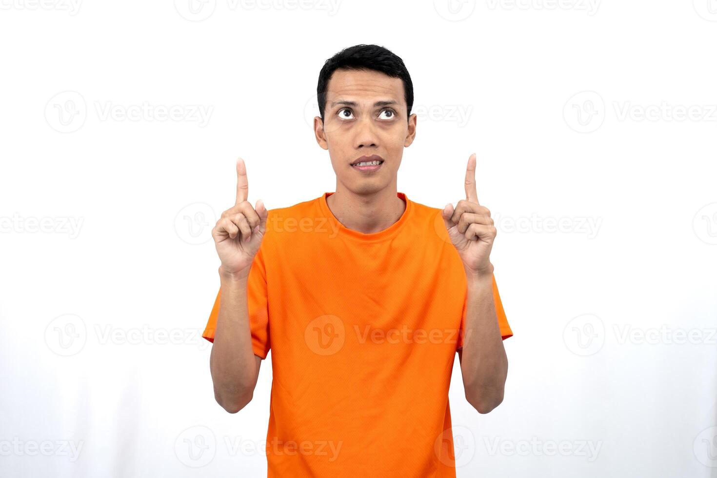 Portrait of a young Asian man wearing an orange t-shirt pointing upwards at copy space for promotional space. isolated on white background. photo
