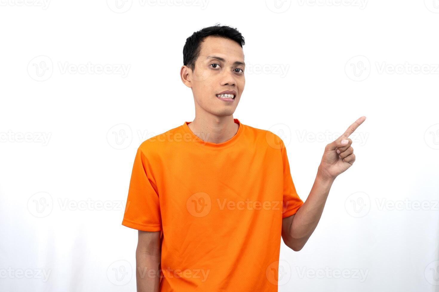 Portrait of a young Asian man wearing an orange t-shirt pointing aside copy space for promotional space. isolated on white background. photo