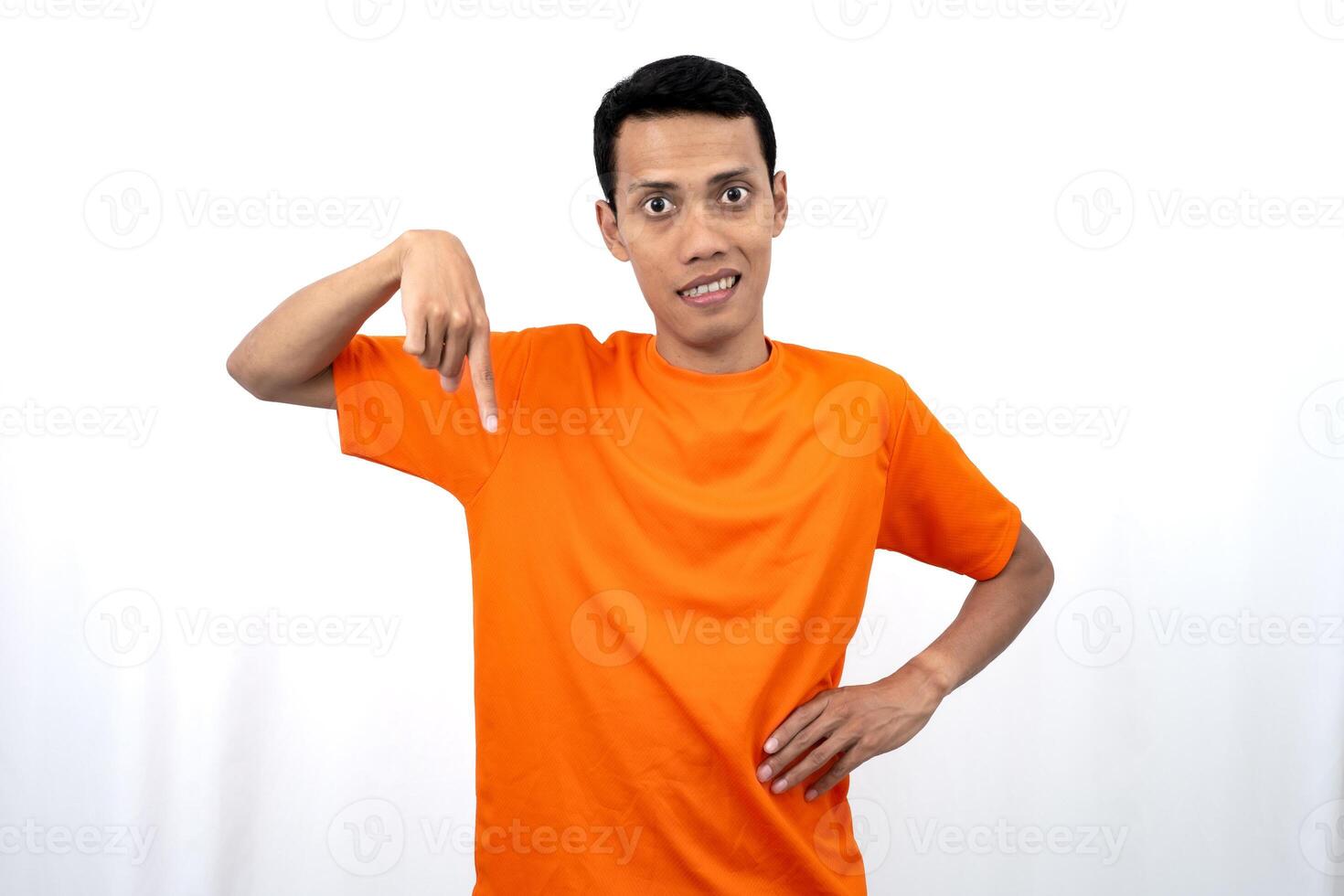 Portrait of a young Asian man wearing an orange t-shirt pointing down copy space for promotional space. isolated on white background. photo