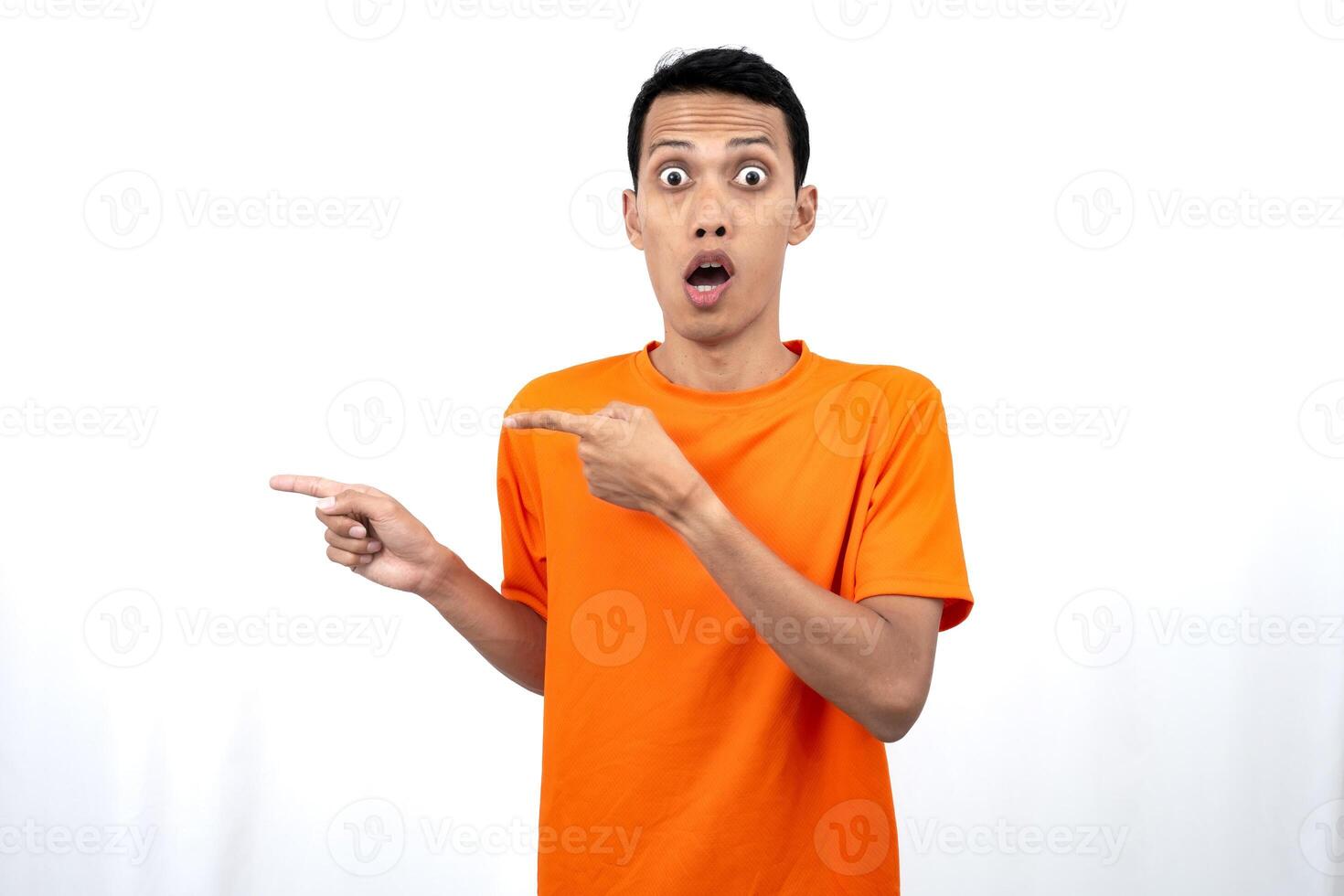 Portrait of a young Asian man wearing an orange t-shirt pointing aside copy space for promotional space. isolated on white background. photo