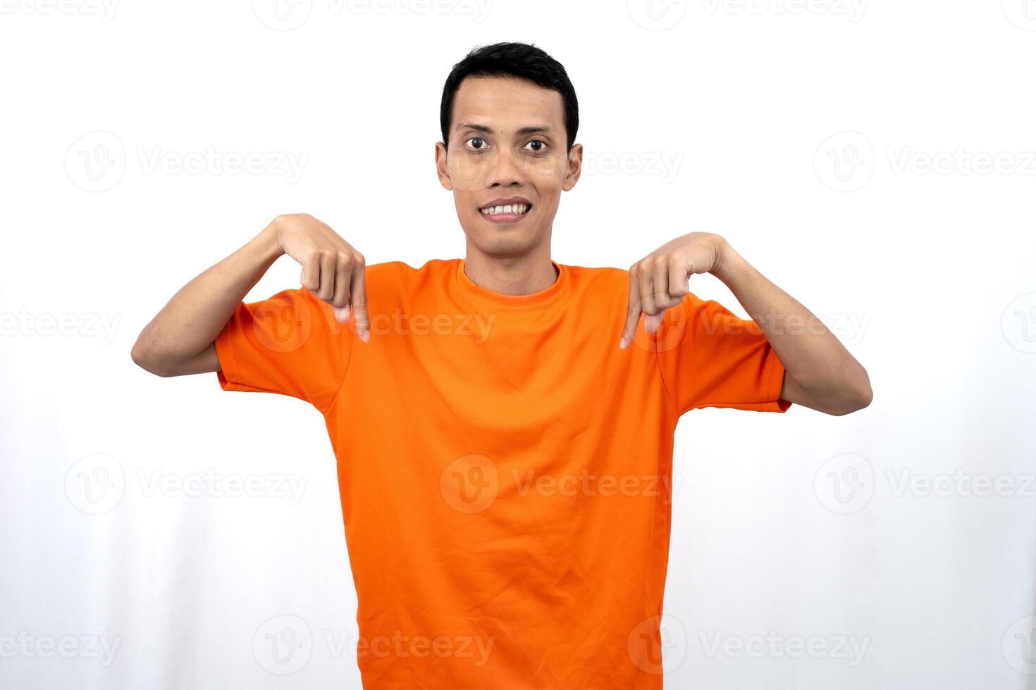 Portrait of a young Asian man wearing an orange t-shirt pointing down copy space for promotional space. isolated on white background. photo