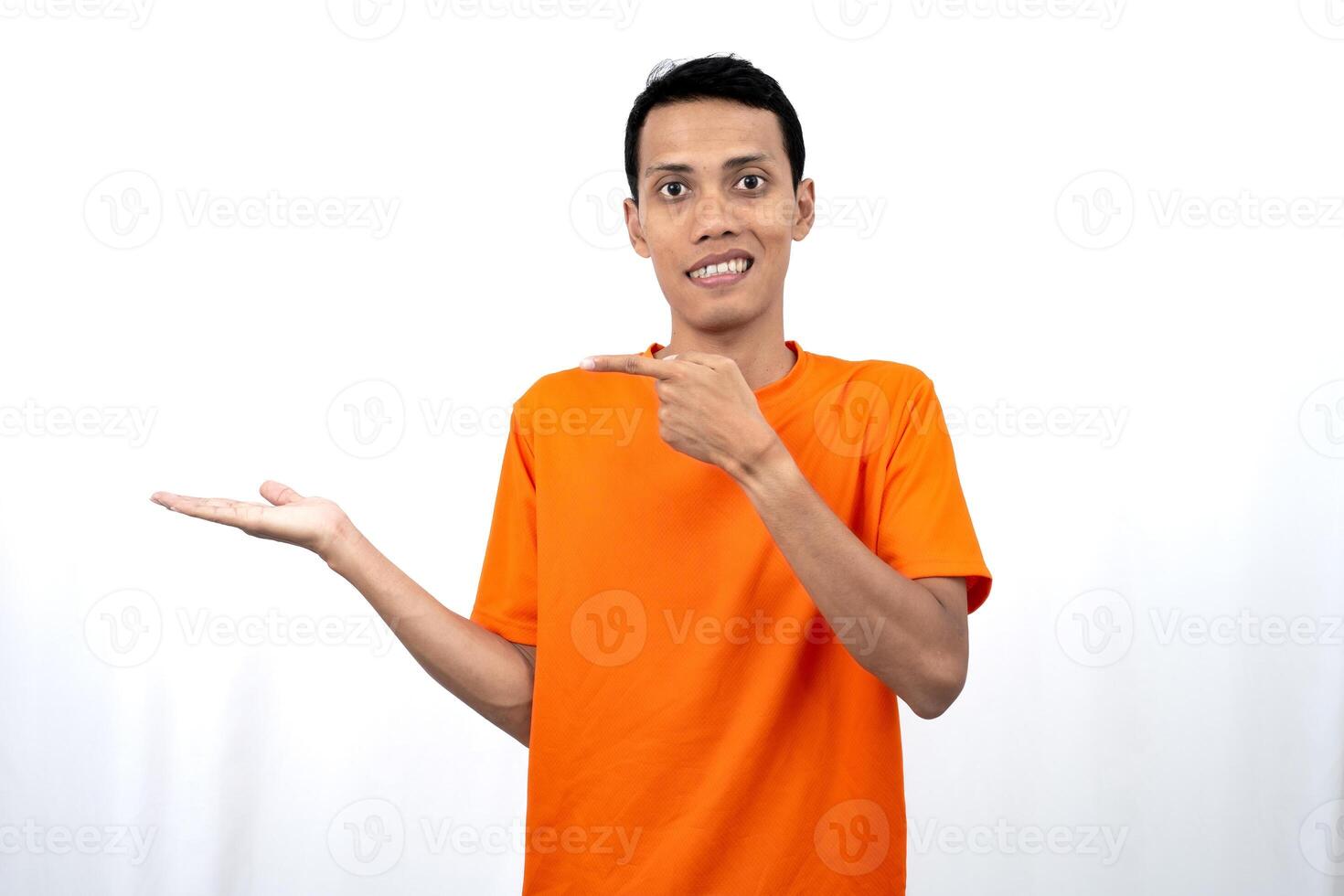 Portrait of a young Asian man wearing an orange t-shirt pointing aside copy space for promotional space. isolated on white background. photo