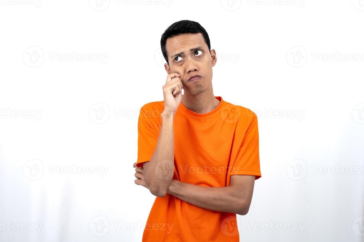Portrait of a young Asian man wearing an orange t-shirt posing thinking, searching for ideas, or confused. Isolated on white background. photo