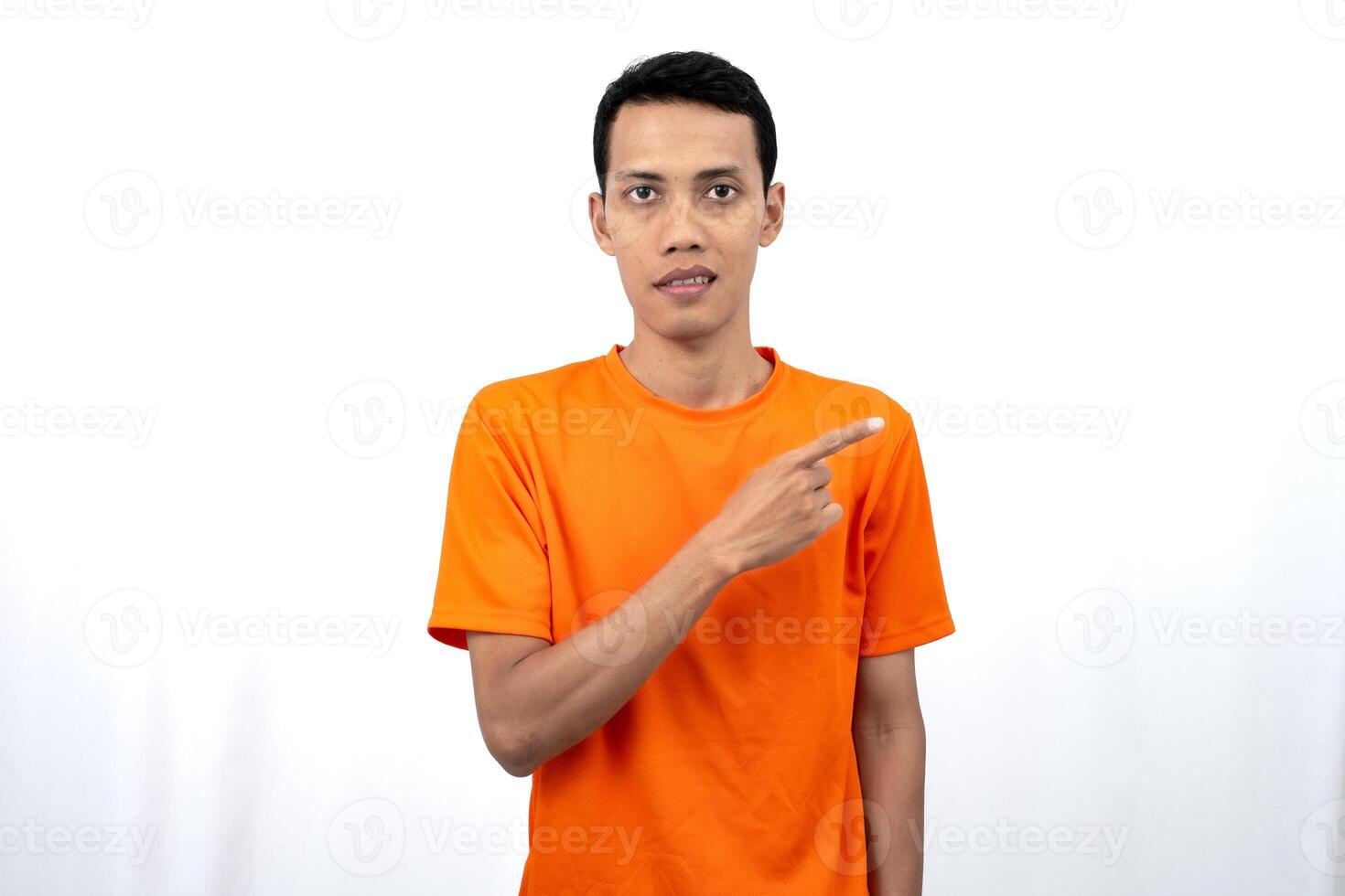 Portrait of a young Asian man wearing an orange t-shirt pointing aside copy space for promotional space. isolated on white background. photo