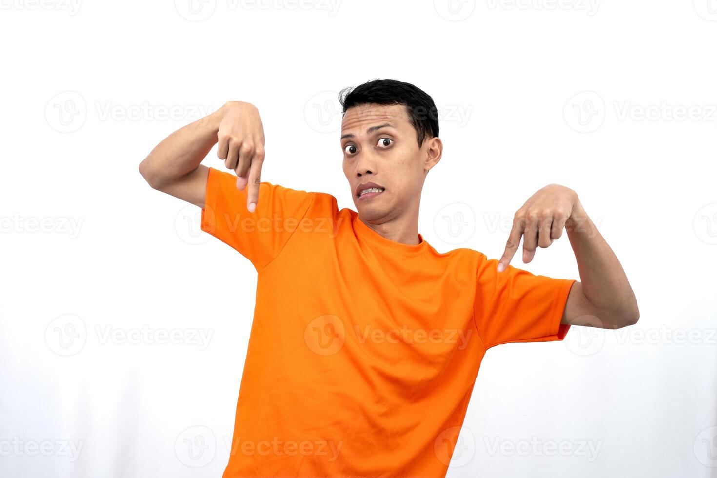 Portrait of a young Asian man wearing an orange t-shirt pointing down copy space for promotional space. isolated on white background. photo