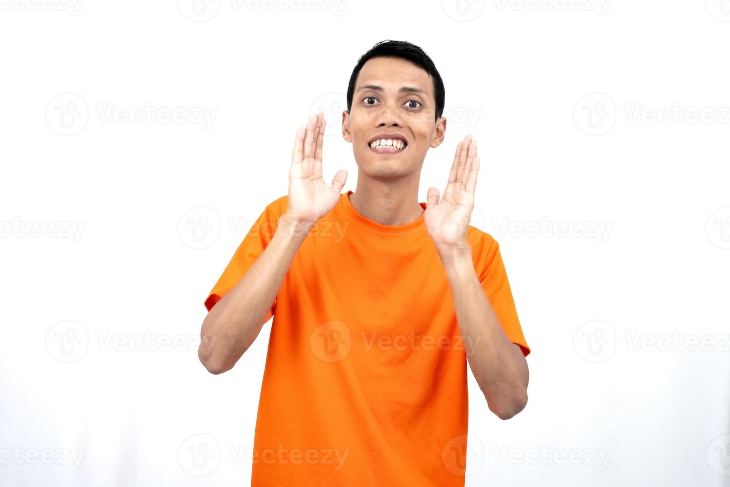 Portrait of a young Asian man wearing an orange t-shirt with his hand near his mouth whispering gossip and telling secrets while sharing news isolated on white background. photo