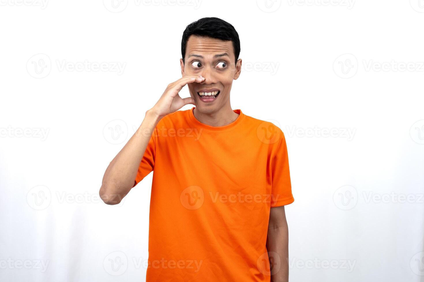 Portrait of a young Asian man wearing an orange t-shirt with his hand near his mouth whispering gossip and telling secrets while sharing news isolated on white background. photo