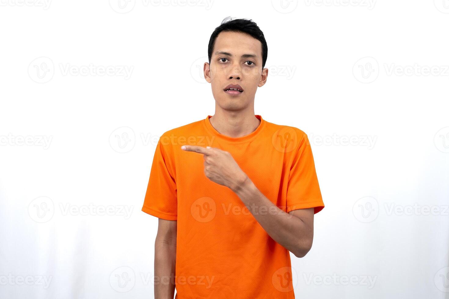 Portrait of a young Asian man wearing an orange t-shirt pointing aside copy space for promotional space. isolated on white background. photo