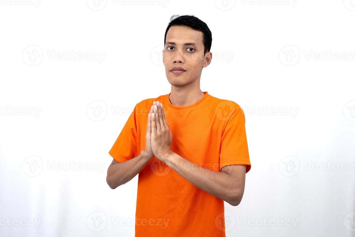 Portrait of a young Asian man wearing an orange t-shirt posing giving a warm greeting to a friend or customer. Isolated on white background. photo