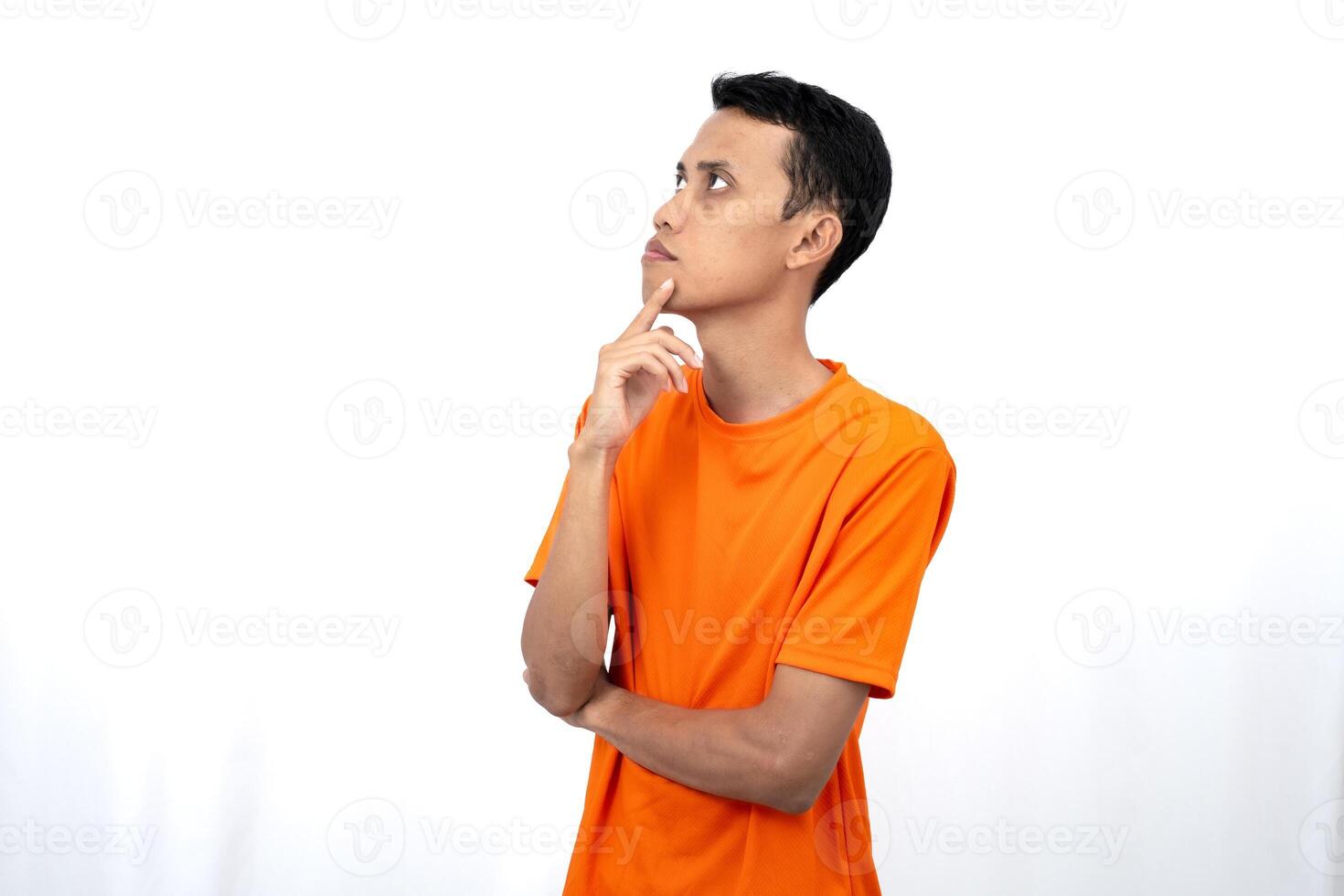 Portrait of a young Asian man wearing an orange t-shirt posing thinking, searching for ideas, or confused. Isolated on white background. photo