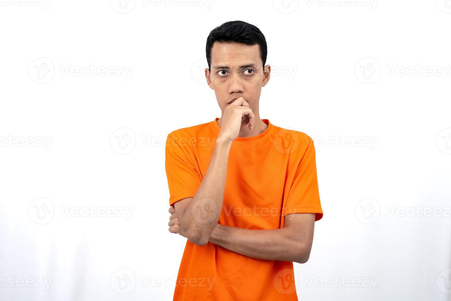 Portrait of a young Asian man wearing an orange t-shirt posing thinking, searching for ideas, or confused. Isolated on white background. photo