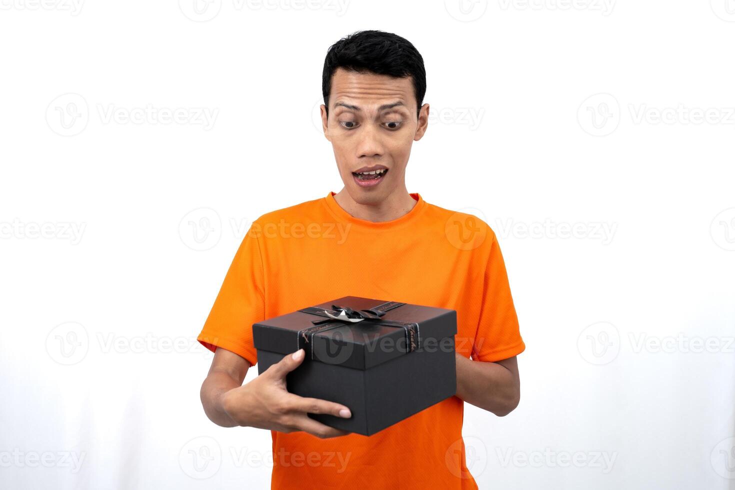 Portrait of a young Asian man wearing an orange t-shirt with a happy expression, surprised to get a gift. Isolated on white background. photo