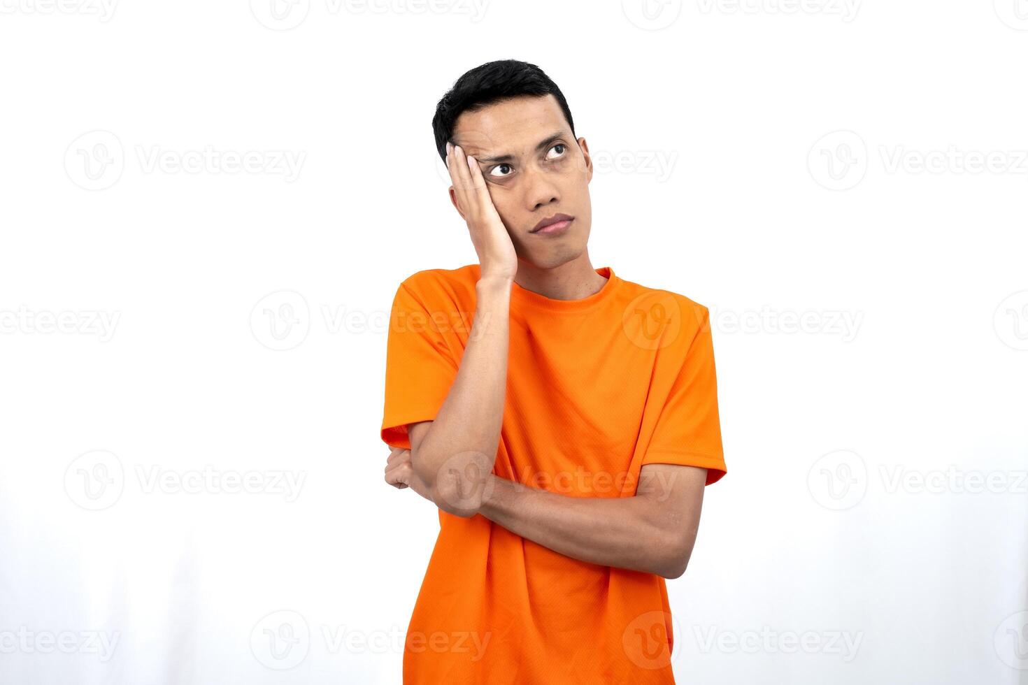 Portrait of a young Asian man wearing an orange t-shirt posing thinking, searching for ideas, or confused. Isolated on white background. photo
