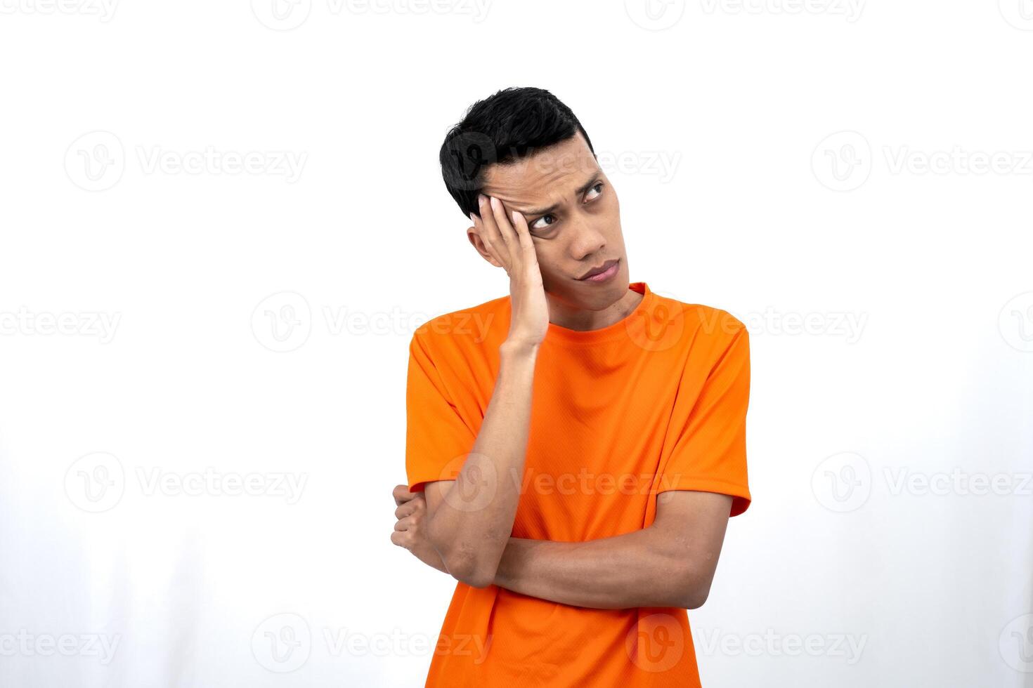 Portrait of a young Asian man wearing an orange t-shirt posing thinking, searching for ideas, or confused. Isolated on white background. photo