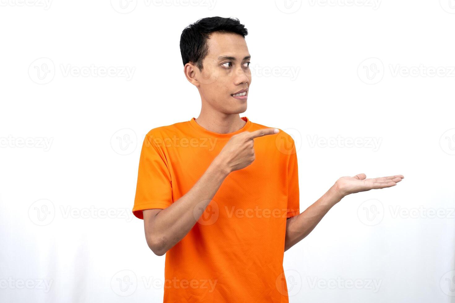 Portrait of a young Asian man wearing an orange t-shirt pointing aside copy space for promotional space. isolated on white background. photo
