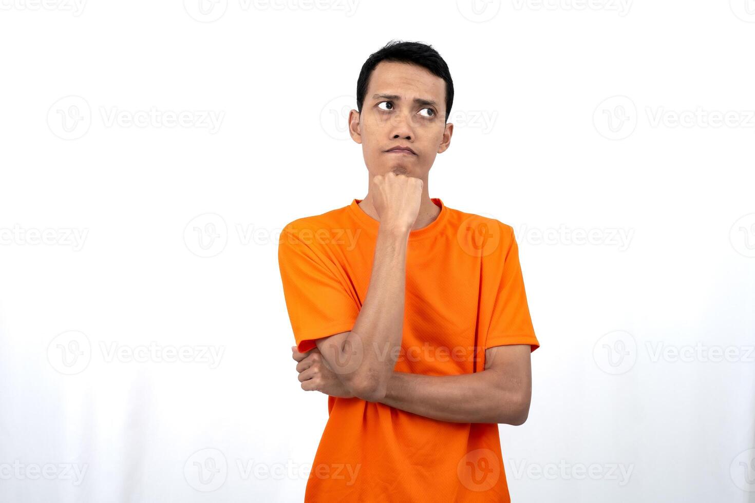Portrait of a young Asian man wearing an orange t-shirt posing thinking, searching for ideas, or confused. Isolated on white background. photo