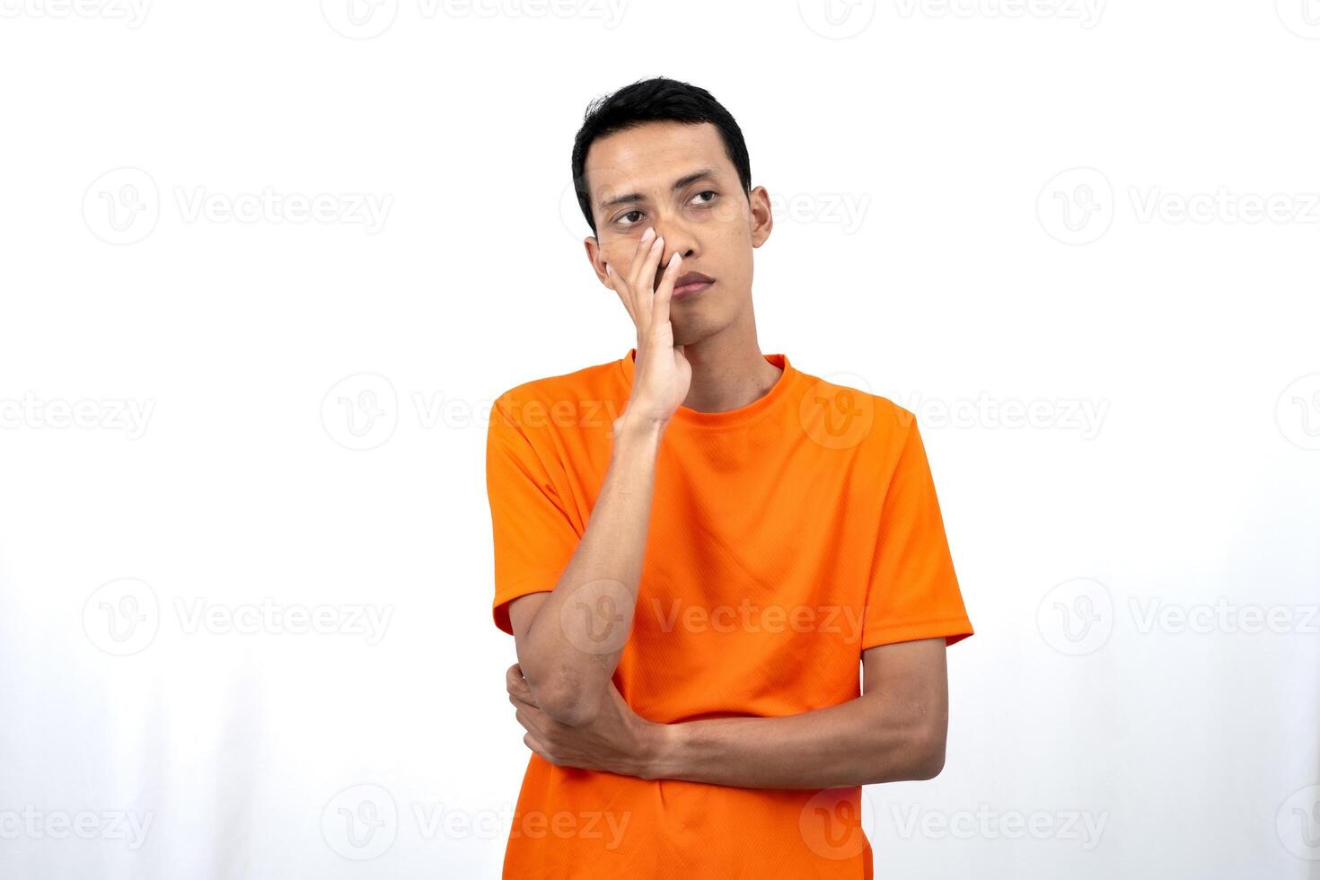 Portrait of a young Asian man wearing an orange t-shirt posing thinking, searching for ideas, or confused. Isolated on white background. photo