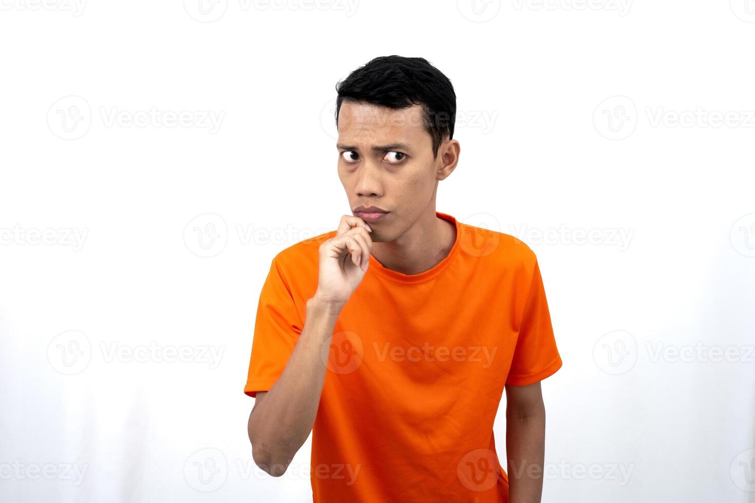 Portrait of a young Asian man wearing an orange t-shirt posing thinking, searching for ideas, or confused. Isolated on white background. photo