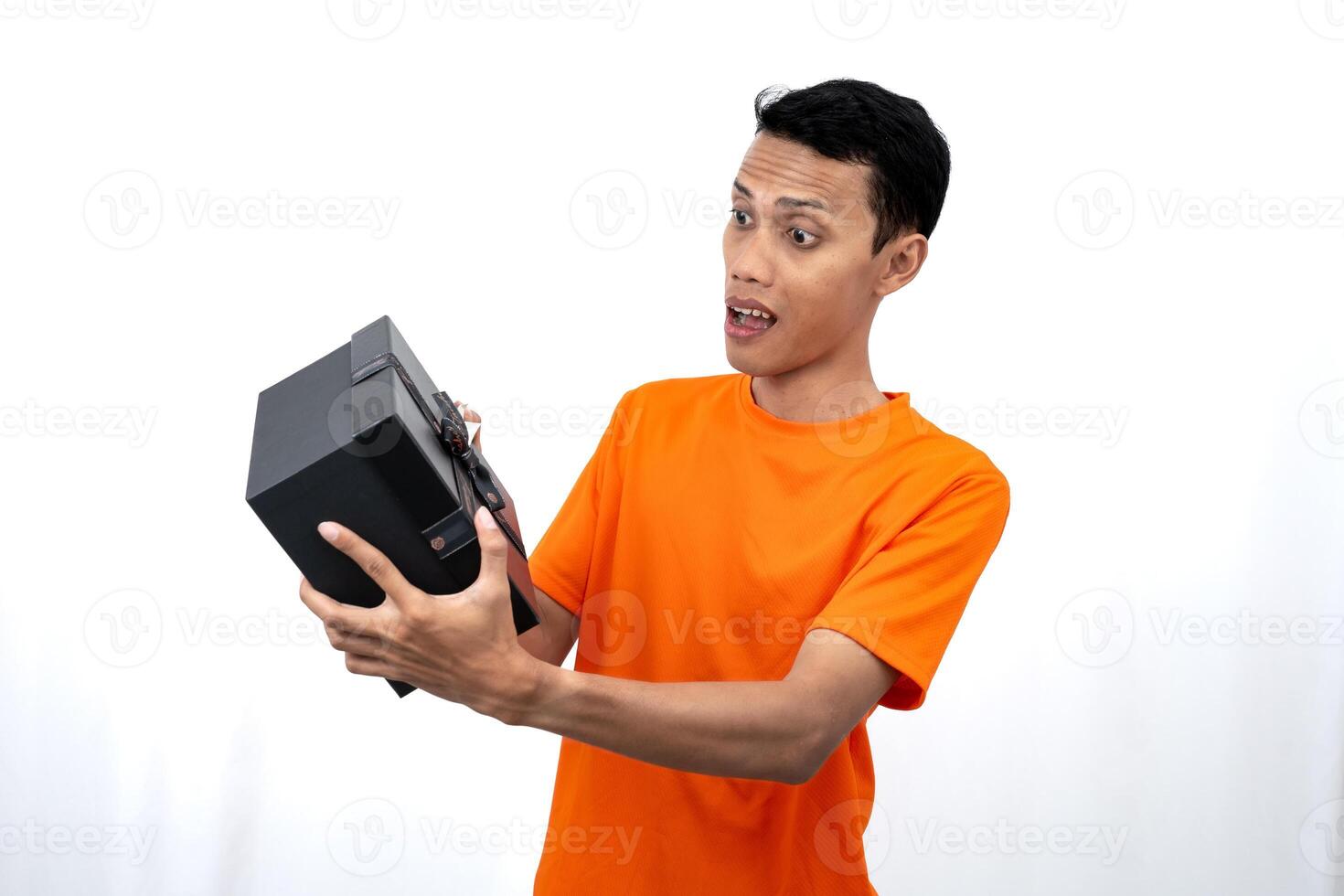 Portrait of a young Asian man wearing an orange t-shirt with a happy expression, surprised to get a gift. Isolated on white background. photo