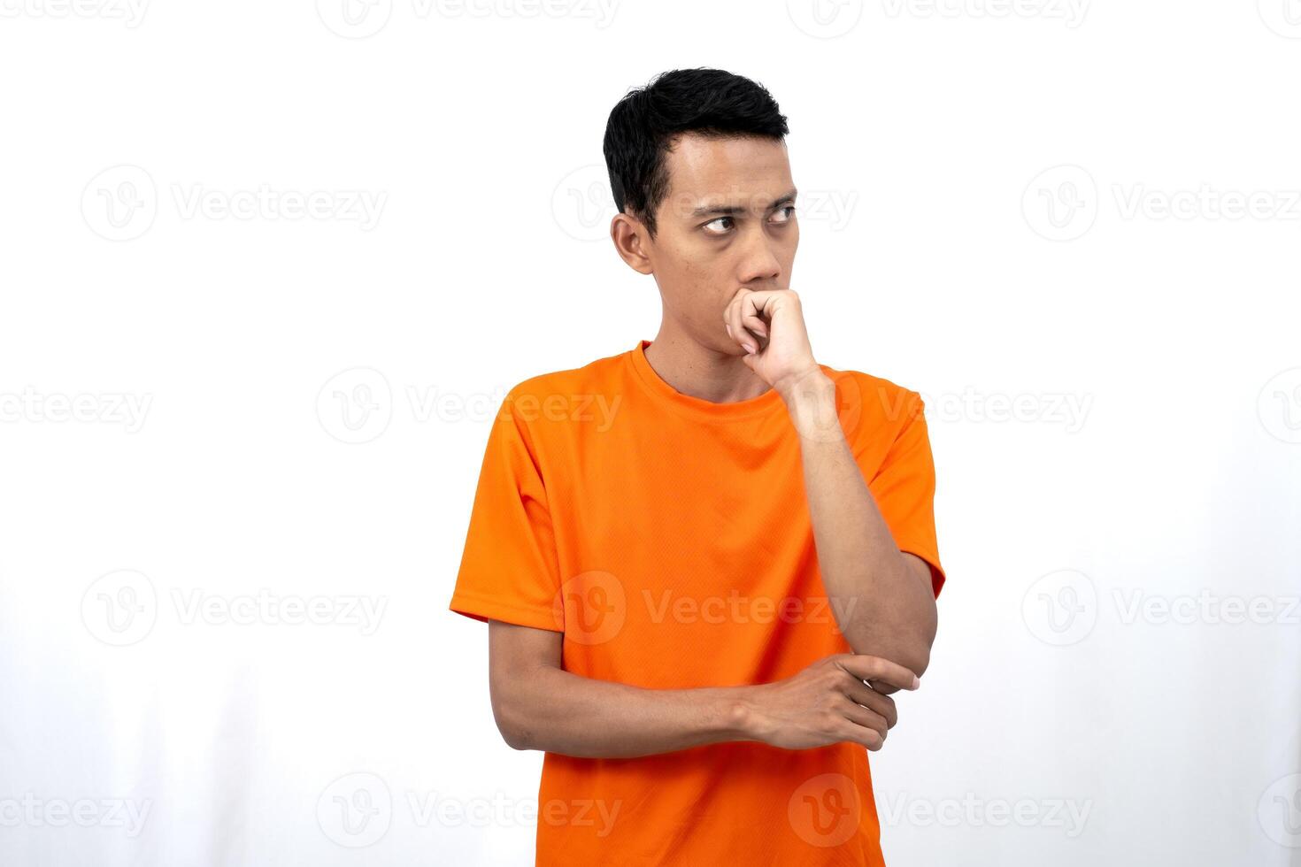 Portrait of a young Asian man wearing an orange t-shirt posing thinking, searching for ideas, or confused. Isolated on white background. photo