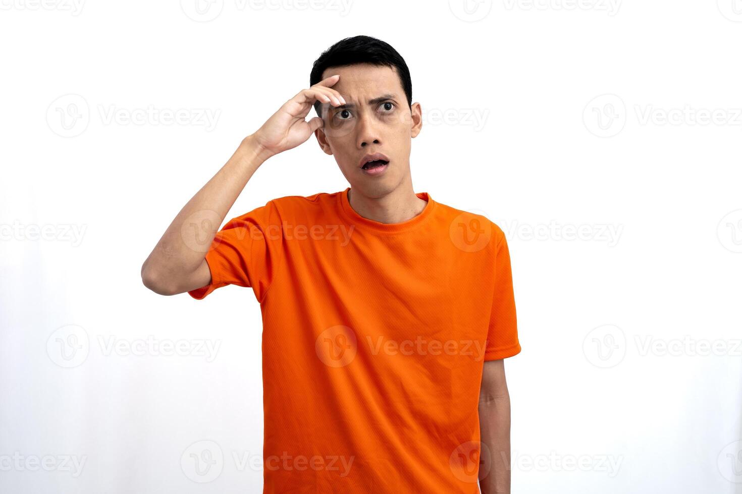 Portrait of a young Asian man wearing an orange t-shirt looking surprised, shocked and shocked. Hands are near eyes, isolated on white background. photo