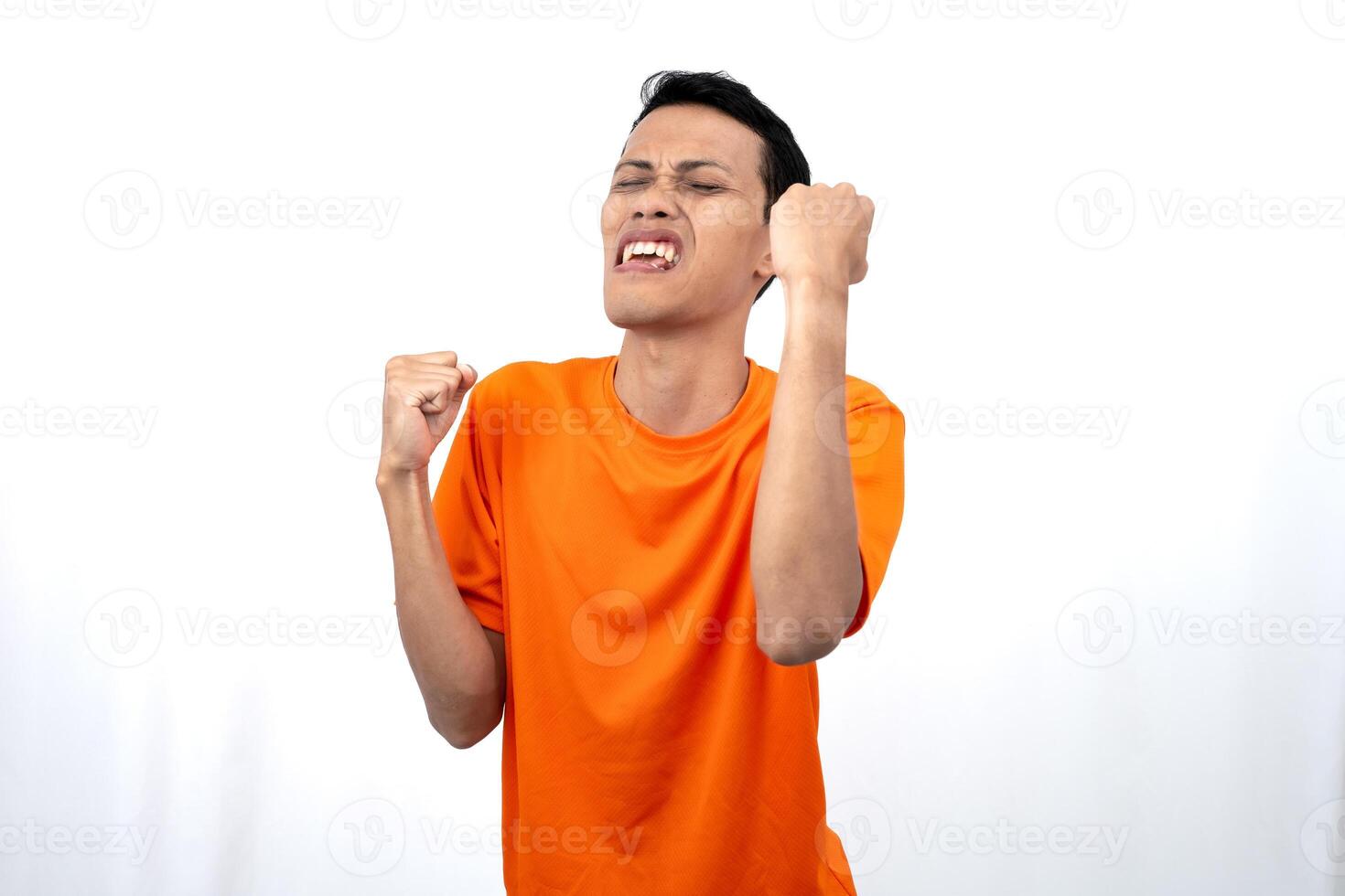Portrait of a young Asian man wearing an orange t-shirt with a happy expression, surprised to get good news. Isolated on white background. photo