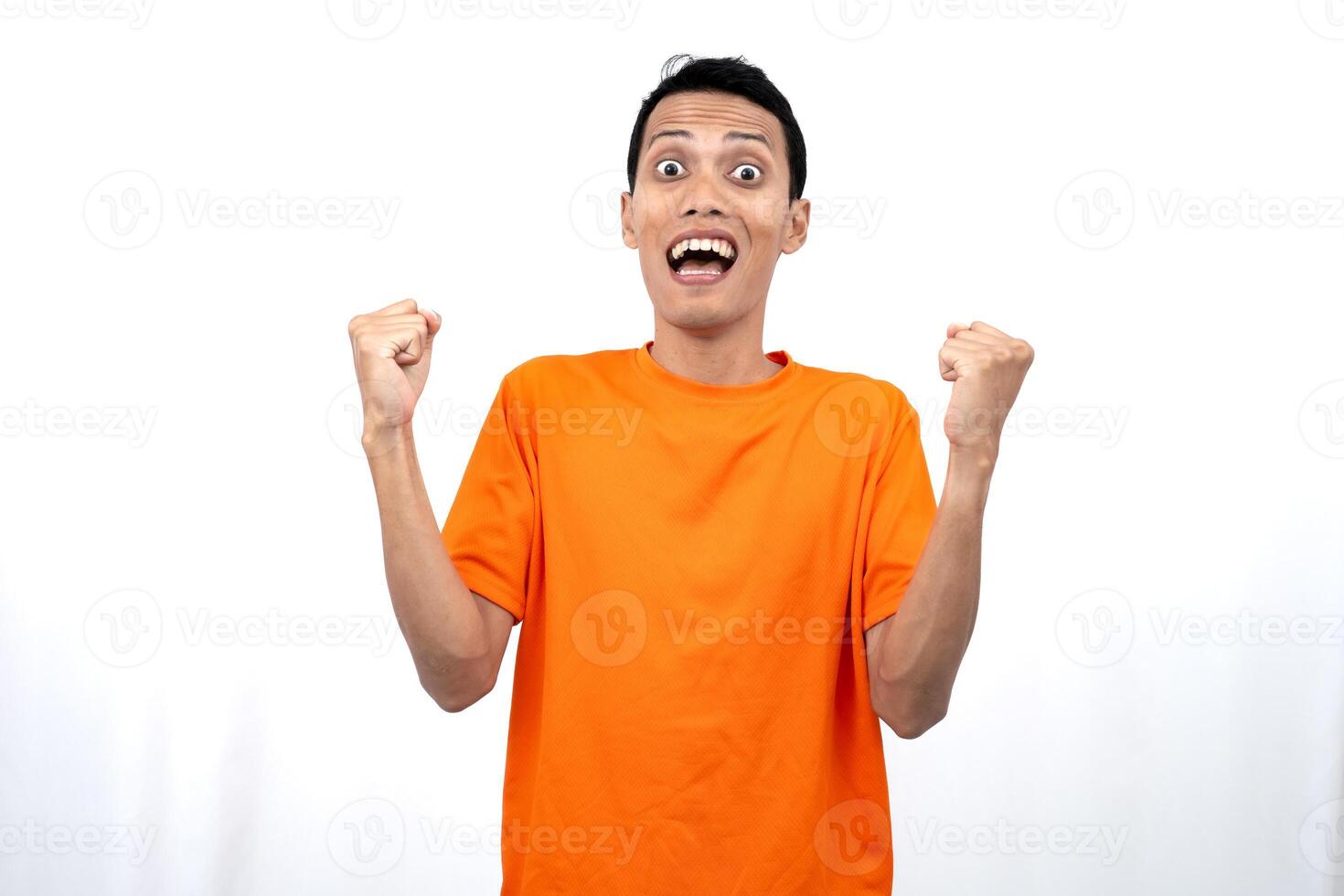 Portrait of a young Asian man wearing an orange t-shirt with a happy expression, surprised to get good news. Isolated on white background. photo