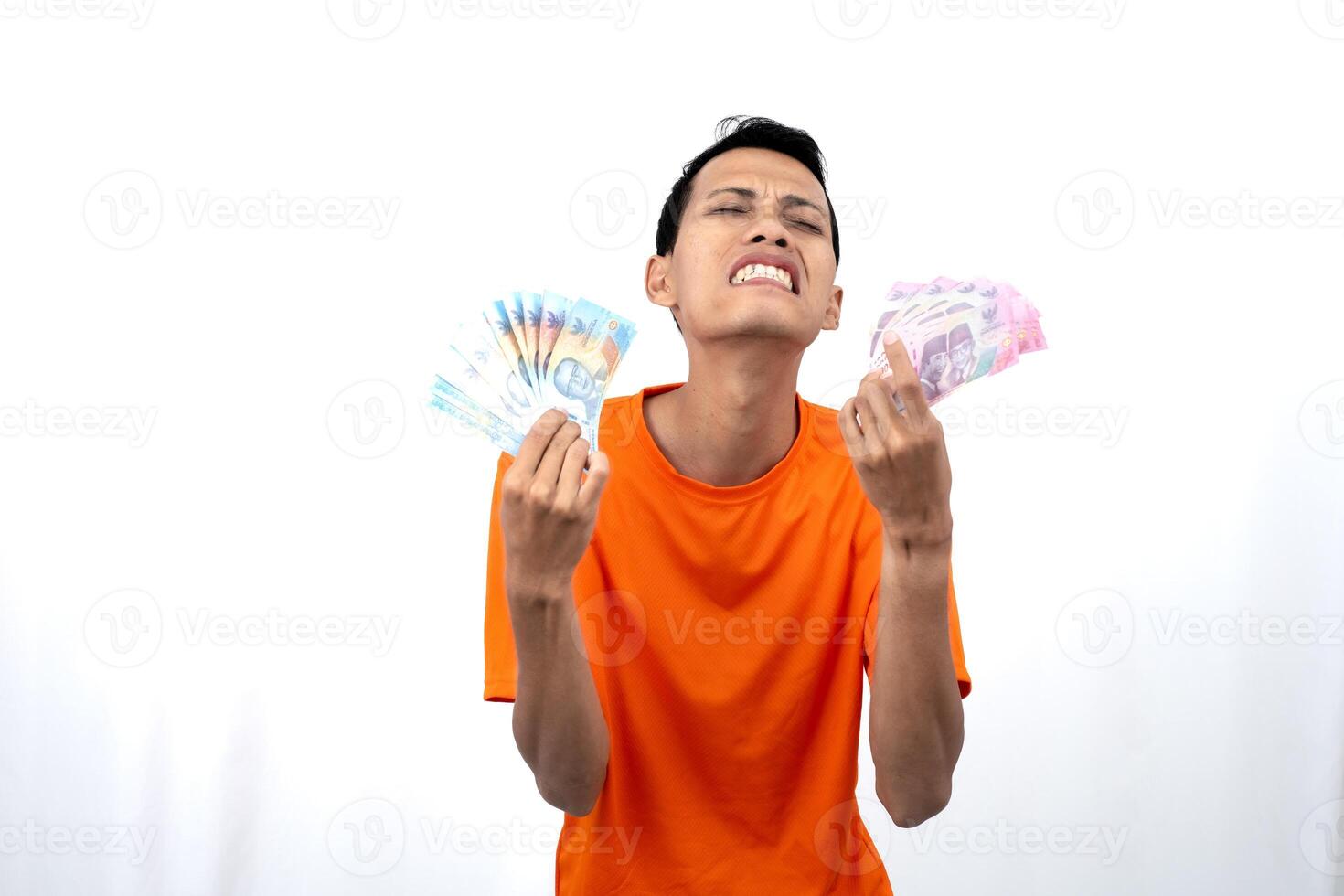 Portrait of a young Asian man wearing an orange t-shirt with a happy, surprised, pleased expression while carrying hundreds of thousands of rupiah. isolated on a white background. photo