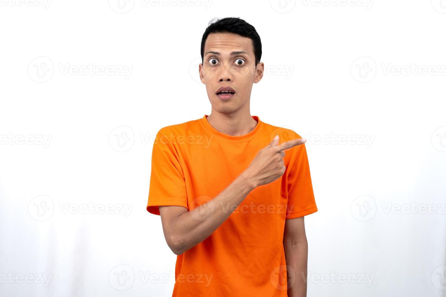 Portrait of a young Asian man wearing an orange t-shirt pointing aside copy space for promotional space. isolated on white background. photo