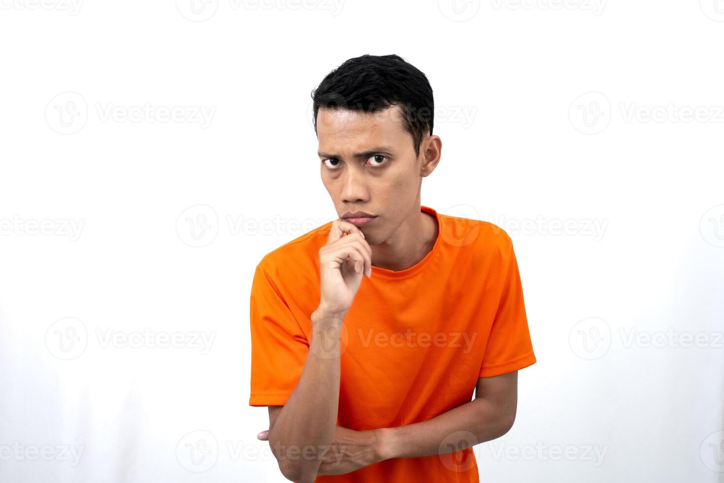 Portrait of a young Asian man wearing an orange t-shirt posing thinking, searching for ideas, or confused. Isolated on white background. photo